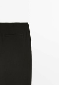 Jupe noire sur mesure avec une poche fendue horizontale sur le côté supérieur gauche, présentée sur fond blanc.