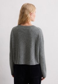 Pull gris court en maille douce, avec un col rond et des manches longues, associé à un pantalon en velours côtelé foncé.