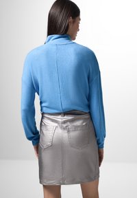 Pullover azzurro chiaro con colletto alto, abbinato a una minigonna metallica argento con tasche posteriori e una texture liscia.