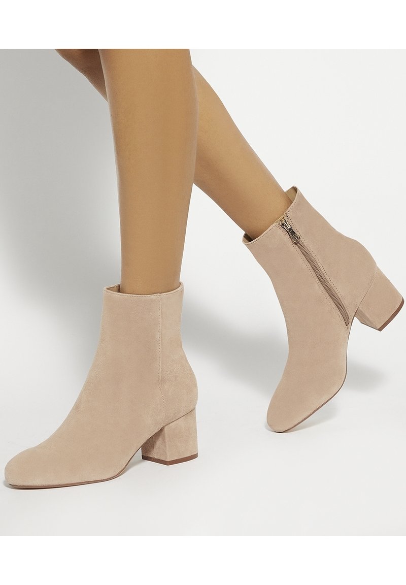 Bottines en daim beige clair avec bout carré et talon bloc. Détail de fermeture éclair latérale pour faciliter l'enfilage. Texture lisse sur toute la surface.