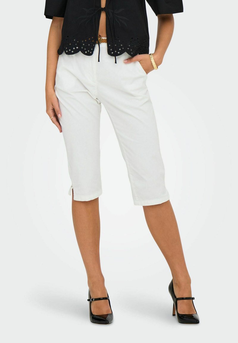 Bijele kratke hlače s dva bočna proreza na rubu, uparene s crnim topom koji ima izvezene detalje i mašnu na izrezu.