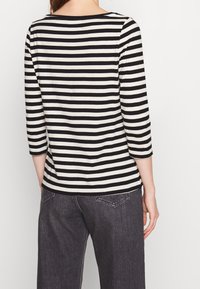 Svart och beige randig långärmad topp med båthals och trekvartsärmar, bärs med mörka jeans. Mjuk, andningsbar tyg.