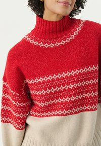 Sweter w czerwono-kremowy wzór z prążkowym golfem. Posiada geometryczne wzory na karczku oraz miękką teksturę. Luźny krój.