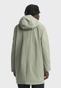 Dlouhá, kapucňová bunda ze světlé zelené látky. Má rovný střih, boční kapsy a minimalistický design bez viditelného kovového vybavení.