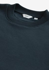 Mörkblå sweatshirt med rund halsringning, ribbad krage och mjuk textur. Varumärkesetiketten "NEXT" syns inuti halsringningen.