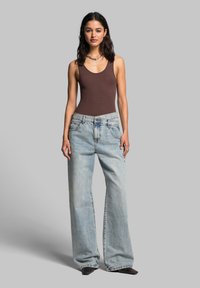 Brown fitted tank top and light blue wide-leg jeans with a faded finish. Silver jewelry accentuates the outfit. Simple, clean design.