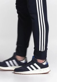 Navy athletic shoes with white stripes, silver accents, and a rubber sole. Paired with navy joggers featuring three white stripes.