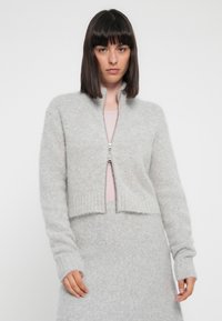 Heled hall cardigan, mille pehmeist ja kohevast kangast, millel on püstine krae, lukuga sulgemine ja soonikkoes varrukate ning ääre osa.