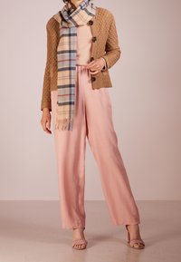 Pantaloni ampi rosa chiaro abbinati a un cardigan beige con texture e a una sciarpa a quadri con accenti blu e rossi. Tacchi rosa con cinturino completano il look.