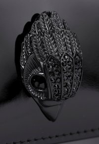 Chiusura di borsa nera con un intricato design a forma di piuma e decorazioni in cristallo nero su uno sfondo lucido nero.