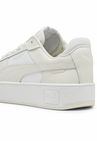 Baskets blanches Puma en cuir texturé, détails cousus, semelle plateforme et logo Puma sur le talon et le côté.