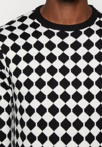 Černobílý pletený svetr s diamantovým vzorem, s žebrovaným kulatým výstřihem a texturovanou látkou.