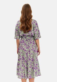 Kvetinové midi šaty v svetlozelennej farbe s fialovým kvetinovým vzorom, zúžený pás a krátke rukávy, s voľnou A-čkovou sukňou. Zozadu.