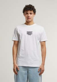 Balta medvilnės marškinėliai su juodu "nyc" logotipu ant krūtinės. Trumpomis rankovėmis ir klasikinė apykakle. Tiesus siluetas.