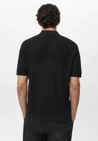 Polo shirt corto a maniche corte nero in maglia con un motivo testurizzato, caratterizzato da un fit rilassato e colletto piatto, abbinato a pantaloni scuri.