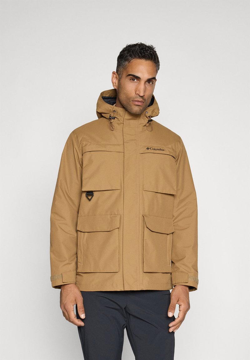 Chaqueta marrón impermeable con capucha, que cuenta con múltiples bolsillos delanteros, puños ajustables y un bolsillo con cremallera. Logo de Columbia en el pecho.