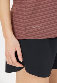 Sneldrogende, kastanjebruine gestreepte sporttop boven zwarte shorts. De top heeft een aangesloten ontwerp met een gladde textuur en een logo aan de zijkant.