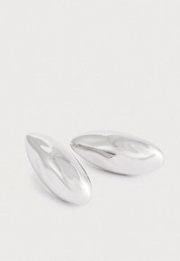 Hladké, lesklé strieborné oválne manžetové gombíky s reflexnými povrchmi ležiace na obyčajnom bielom pozadí.