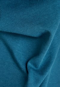 Teal- värinen neulottu kangas, jossa on ribbitekstuuri ja pehmeä, sileä pinta, taitettuna paljastaen syvyyttä ja ulottuvuutta.