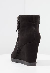 Bottines noires à talon en daim doux, avec une fermeture éclair sur le côté et des détails cousus, dotées d'une semelle en caoutchouc texturé pour une bonne adhérence.