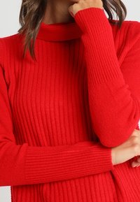 Punainen ribattuja neulepaita, jossa on korkea kaula-aukko ja pitkät hihat; siinä on pehmeä rakenne ja slim fit -muotoilu, joka korostaa lämpöä ja mukavuutta.