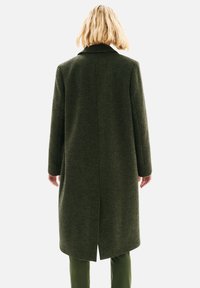 Manteau vert à carreaux avec col, manches longues et coupe droite, doté d'une fente centrale au dos et d'une texture de tissu lisse.