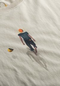 T-shirt beige clair avec une figure peinte marchant avec une casquette orange, une chemise noire et un pantalon sombre. Comprend des accents de couleur.