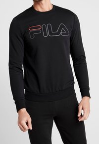 Černá mikina vyrobená z hladkého materiálu. Má kulatý výstřih, dlouhé rukávy a velké logo FILA v šedé a červené barvě na přední straně.