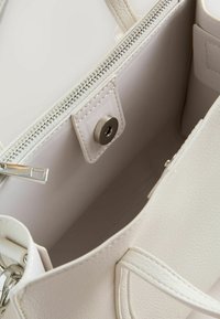 Innenraum einer weißen Handtasche aus Kunstleder mit Reißverschluss, ausgestattet mit einer glatten Textur und einem Druckknopfdetail auf dem Futter.