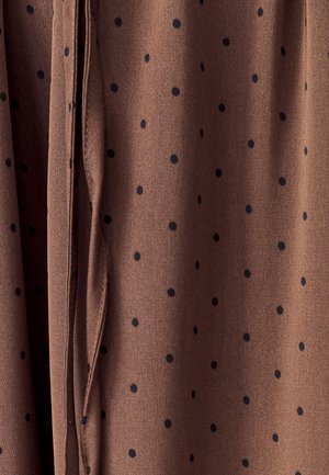 Hnedá tkanina s čiernymi bodkami, ktorá má mäkkú textúru a zavesené záhyby pre drapériu. Podrobné prešívanie pozdĺž okrajov.