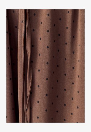 Brunt stof med sorte prikker, med en blød tekstur og hængende folder for drapering. Detaljeret syning langs kanterne.