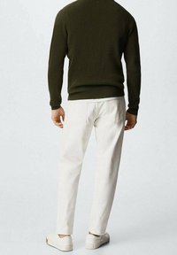 Pull en maille côtelée vert foncé associé à un pantalon fuselé couleur crème et des baskets blanches vus de dos. Design minimaliste.