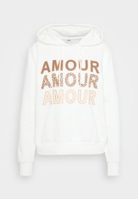 Balts kapuces džemperis ar auklītēm, uz kura krūtīm trīs reizes ir attēlots vārds "AMOUR" dažādās bežās un brūnās krāsās.