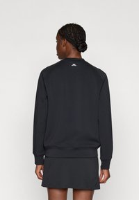 Fekete pulóver kerek nyakkal és bordázott mandzsettával, kis fehér logóval a hátulján. Puha, sima anyag; laza fazon.