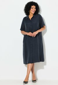 Námořnické šaty s krátkými rukávy a knoflíky, vyrobené z lehké texturované látky, ke kolenům a s bočními kapsami. Úplně doplněné černými botami s špičatou špičkou.