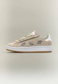 Bež tenisica od brušene kože s izvezenim tamnosivim motivima listova, bijelim naglascima i potplatom od gume boje gume; zaobljeni vrh i ravno vezanje.