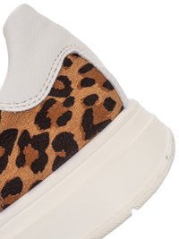 Primer plano del talón de una zapatilla que presenta una parte superior de cuero blanco con un panel de tela con estampado de leopardo en marrón y negro, y una suela gruesa de goma blanca.