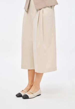 Scarpe basse beige con punta nera, caratterizzate da una sottile fascia sul dorso del piede e una superficie in pelle liscia.