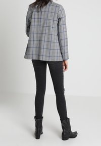 Šedý kostkovaný sako s modrými akcenty, vrstvené přes černé slim-fit džíny, doplněné kotníkovými botami. Měkká tkanina, strukturovaný design.