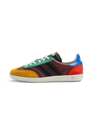 Baskets basses avec semelle blanche, panneaux multicolores en jaune moutarde, vert, bordeaux, rayures noires, talon rouge et col bleu avec lacets blancs.