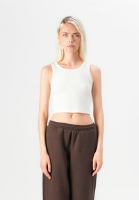 Hvit ribbet tank topp med rund hals, parret med brune løstsittende joggebukser med elastisk liv.