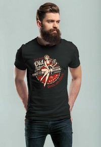 Schwarzes Baumwoll-T-Shirt mit einem Vintage-Graphic einer Frau in einem roten Kleid, umgeben von mechanischen Elementen und fettem Text in Rot und Creme.