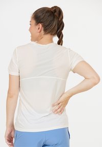 Hvid sports t-shirt med korte ærmer og en semi-transparent mesh øverste sektion, parret med blå bukser, der viser et tætsiddende design.