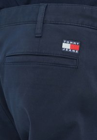 Marineblauwe Tommy Jeans broek heeft een achterzak met een rechthoekige logopatch. De stof heeft een gladde textuur en een getailleerd ontwerp.