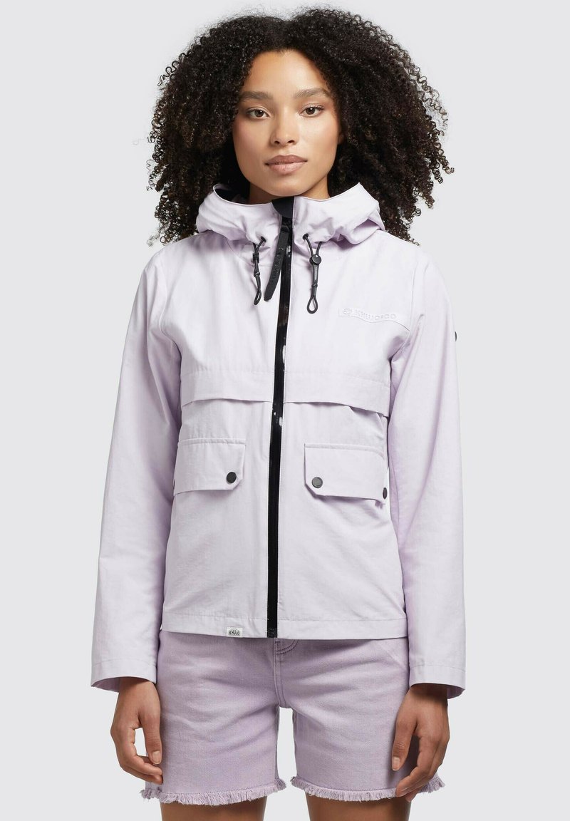 Jachetă zip-up de culoare violet deschis, cu două buzunare frontale, glugă ajustabilă și fermoar negru. Purtată cu pantaloni scurți asortați de culoare lavandă.