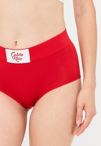 Crvene pamučne hipster gaće s širokim elastičnim pojasom na kojem se nalazi Calvin Klein logo; glatka tekstura; klasični kroj.