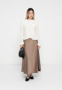 White knitted cardigan with a textured pattern, beige satin skirt, black bag, and black flats. Smooth fabric and relaxed fit.