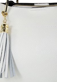 Sac à main en cuir blanc texturé avec des ferrures dorées et un accent de pompon gris. Dispose d'une fermeture éclair sur le dessus.