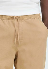 Beige bomull joggebukser med elastisk midjebånd, snorlås og sidelommer. Myk tekstur med sømdetaljer.