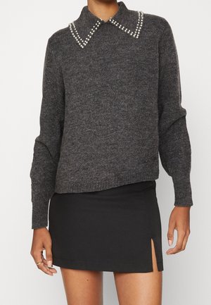 Pull en maille gris foncé à manches longues et col orné de perles blanches, associé à une mini-jupe noire fendue sur le côté.